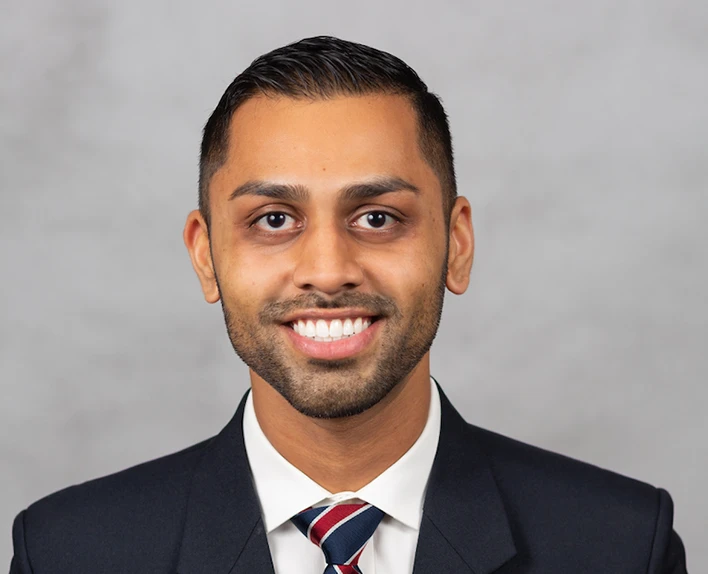 Professional man in dark suit and plaid tie standing against white background.